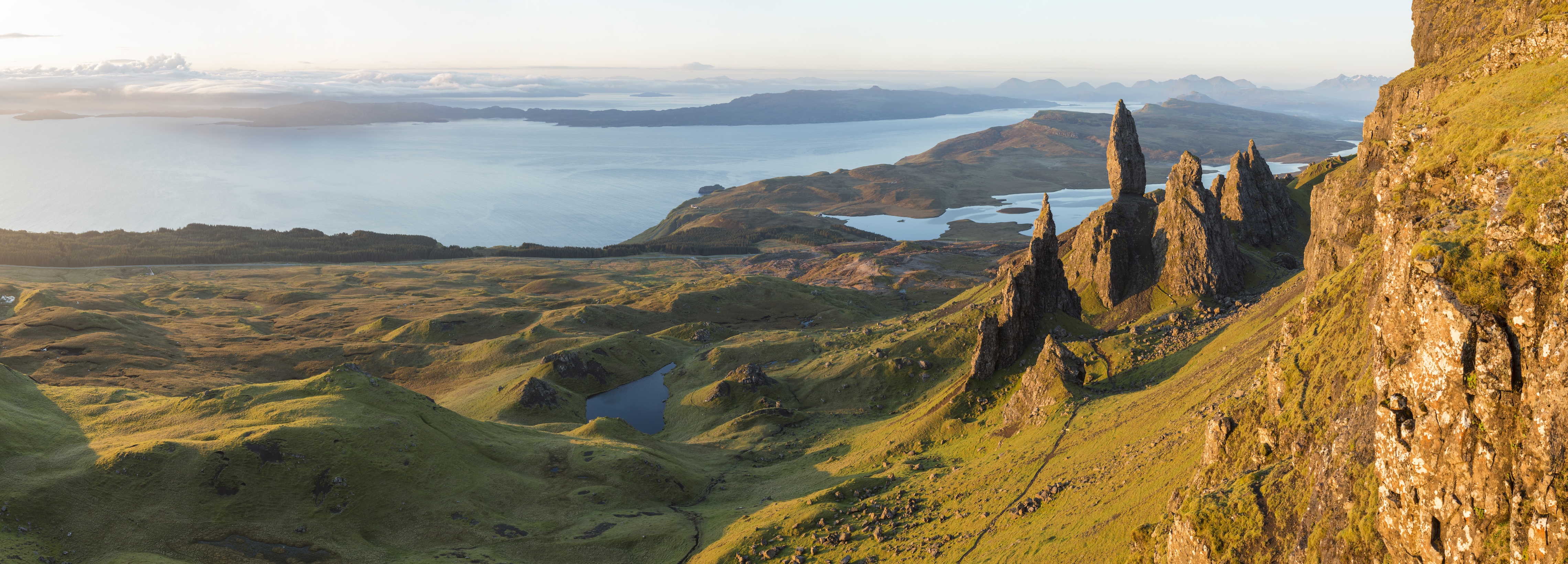 Panoramic landscape view with mountains and large pinnacle rocks, coastline in the distance.